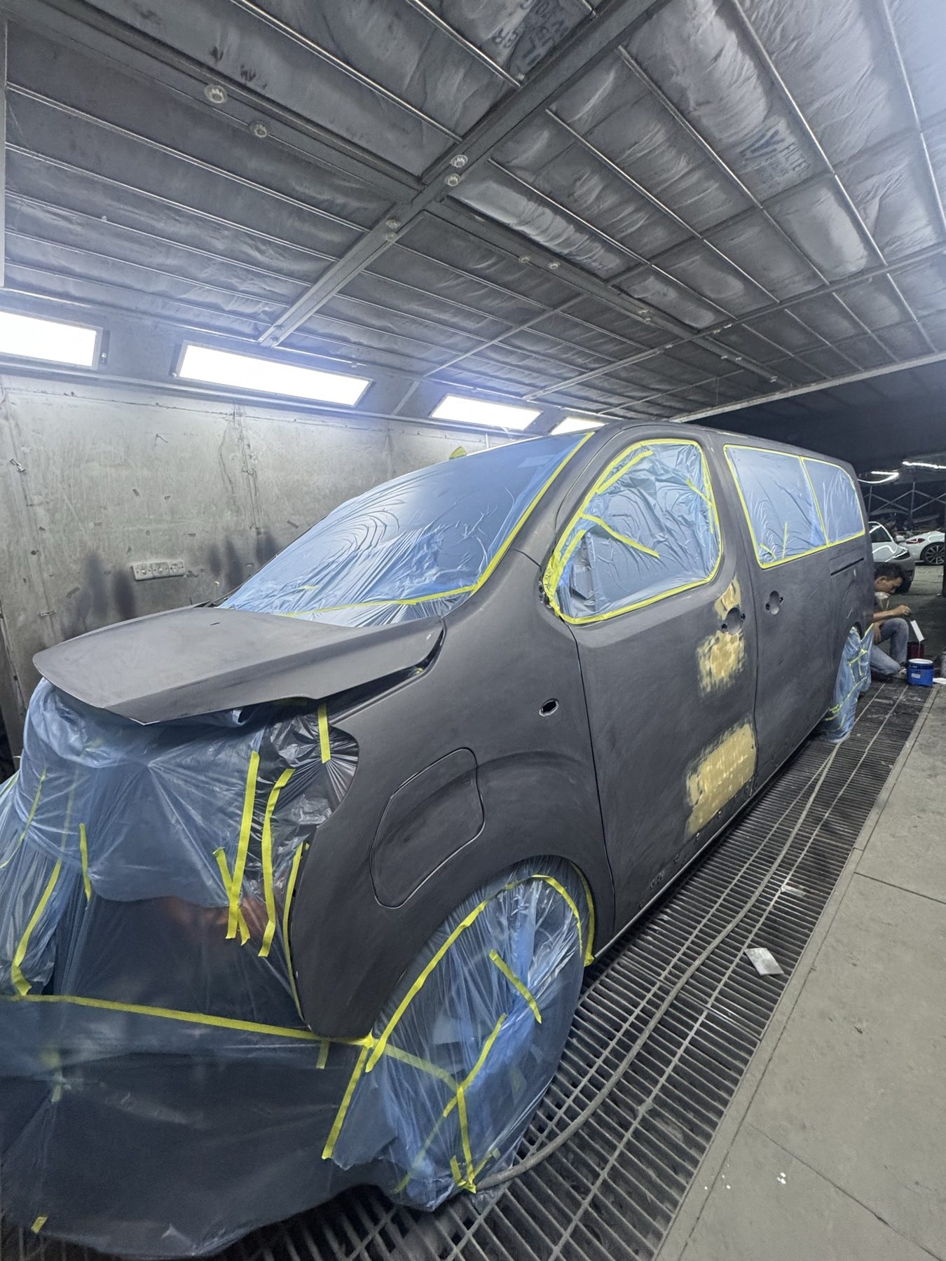 Peugeot Traveller 喺焗漆房內打磨階段，車身呈啞黑色，窗框用黃色膠紙遮蓋